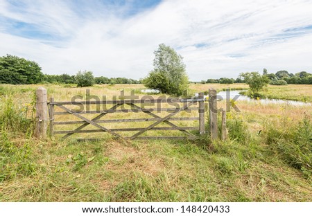 Wooden gate locked with padlock and chain in a nature area next to a curved river.