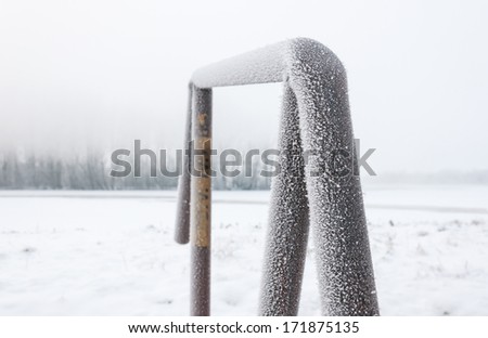 Closeup of frozen ice crystals on an iron pipe in a snowy landscape on a foggy day at dawn.