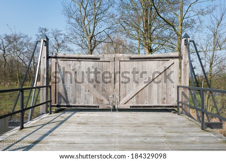 Closed wooden gate at a wooden bridge with a steel balustrade equipped with mesh screen.