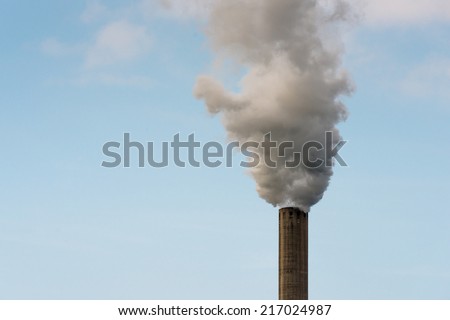 Closeup of dirty dark smoke clouds from a high industrial chimney against a clean blue sky