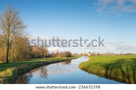 Polder landscape in the Netherlands with a small meandering river on a sunny day in the fall season.