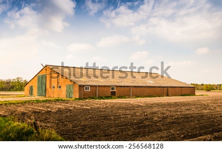 Old brick barn with a corrugated roof and green painted wooden doors. In the foreground a field with the ridges of newly sown potatoes.