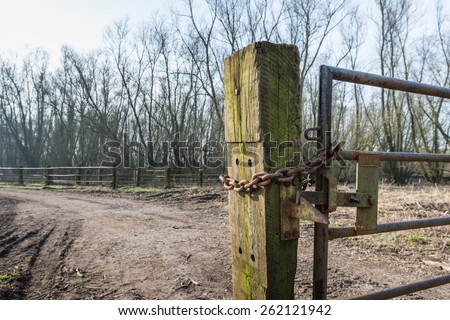 Part of a crooked old gate mounted on an oak railway sleeper. The rusty iron gate is closed and locked with a chain and a padlock.