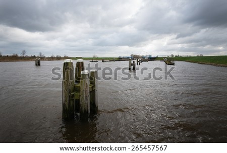 Wooden bollards in a rough river during stormy weather with ominous clouds on the dark sky.
