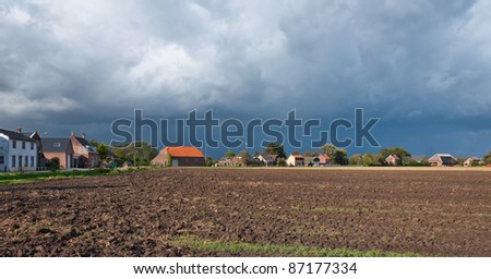 A cloudy sky and a plowed field on the outskirts of a village in the Netherlands