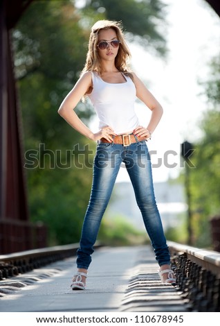  brunette girl in jeans and a t-shirt posing on railroad tracks