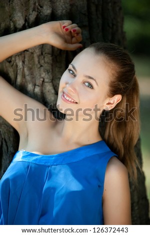 Beautiful brunette girl posing leaning against a tree in the park