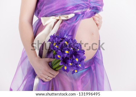 Closeup image of pregnant woman tummy with bouquet of iris on white background