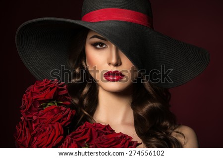 Portrait of a beautiful woman in a black hat with red roses on the shoulders. Red Lips. Beautiful Hair.
