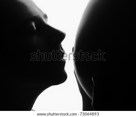 man kissing pregnant belly of his wife. black and white silhouette