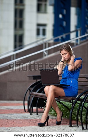 attractive stylish lady with laptop sitting on a bench in the city