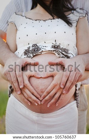 Couple with both hands over the belly making heart shape