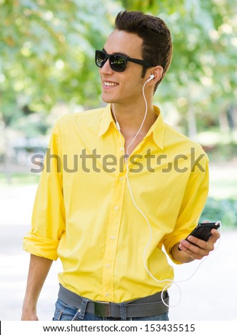 Young cute male listening music on the park with yellow shirt