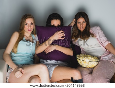 Three young girls at sofa looking a scary movie at TV
