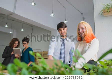 Man and woman pointing at laptop, while partners work hard on a tablet