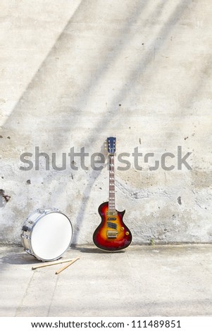 electric guitar and drum in front of a vintage wall