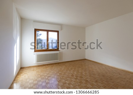 Interior of a empty room with just a window. We can see a small radiator and the floor with wood