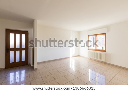 The entrance to the house. Living room consists of the entrance door and the light tiled floor. On the right, instead, there is a window with a radiator underneath.