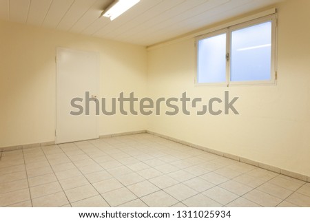Spacious empty cellar. The room is composed of a light tile floor. In front of us there is an exit door and instead a window on the right.