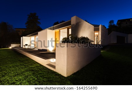 beautiful modern house in cement, view from the garden, night scene