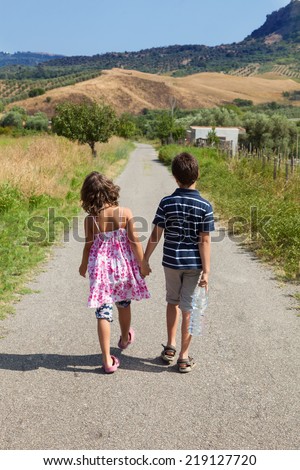 brother and sister walking on the road outdoor with a bottle of water, together , holding hands