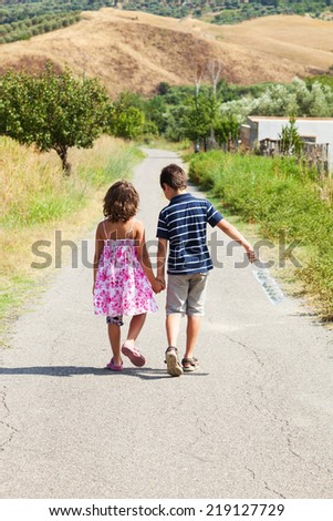 brother and sister walking on the road outdoor with a bottle of water, together , holding hands