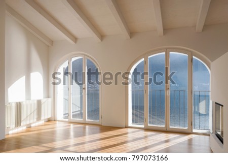 Empty room with large window overlooking the lake. Antique beams on the ceiling of a renovated apartment