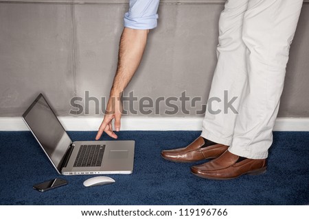 Man standing trying to reach laptop in office - landscape interior.