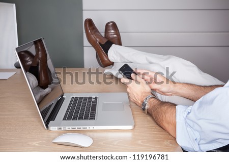 Man in office with feet on desk and laptop - landscape interior.