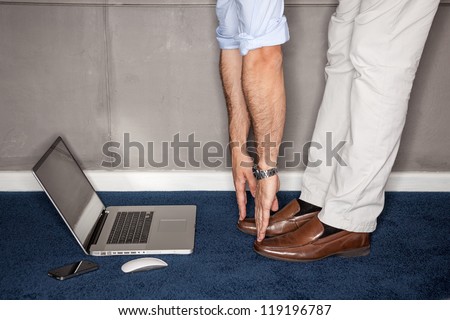 Man standing in office doing exercises with laptop - landscape interior.