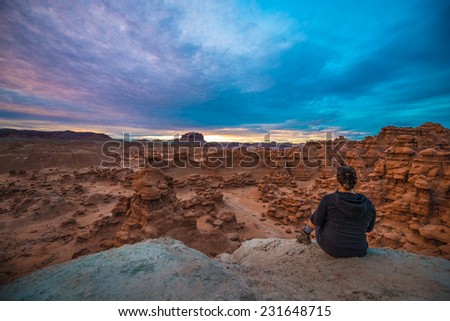 Girl Hiker looking at changing Colorful Sunset Clouds over the Goblin Valley Utah
