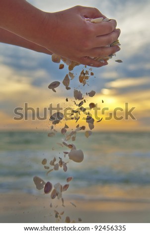 Female hands dropping seashells and sand against beautiful beach sunset