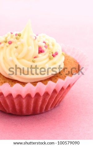 Homemade cupcake, or fairy cake, with buttercream and sprinkles in a pink cup with a pink background