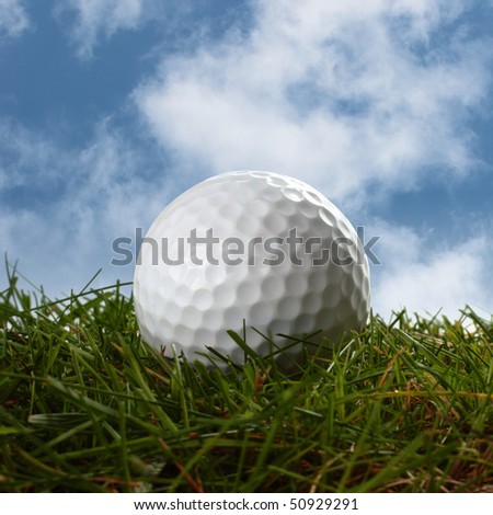 golf ball laying in grass with a cloudy blue sky behind
