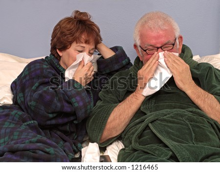 Man and woman in bed blowing noses