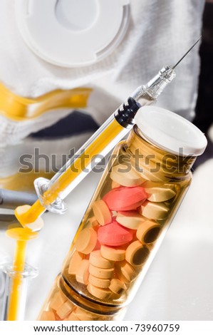 Medicine glass bottle with pills and syringe with protective mask in background