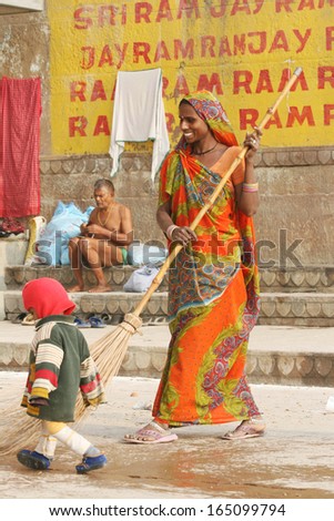 VARANASI, INDIA - NOVEMBER 28: A woman street sweeper watches her son on November 28, 2008 in Varanasi, India. In India streets are kept clean by armies of men and women armed with brooms.