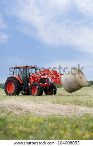 Tractor hauling a round bale an open field with blue sky.