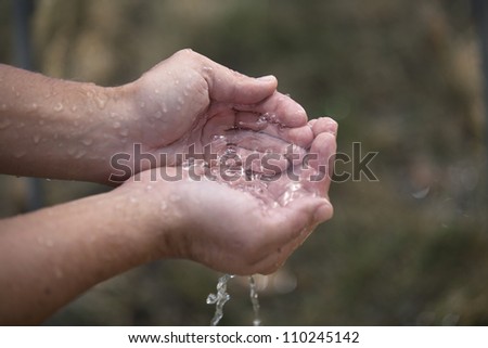 A pair of hands are cupped as they hold clear, trickling water.