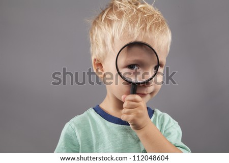A cute young boy holds a magnifying glass up to his eye.