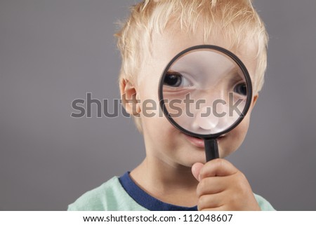 A young boy smiles and holds a magnifying glass up to his face.