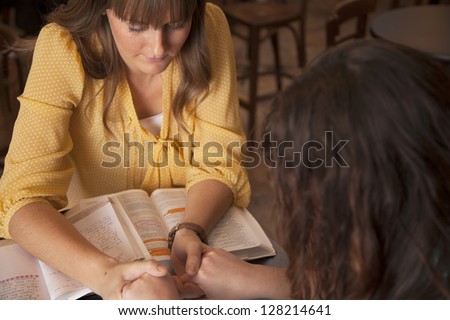 Two women hold hands and pray as they study the bible.