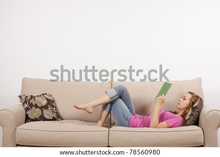 Young woman lying down on the couch enjoying a book.
