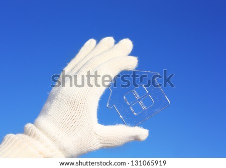 Hands in white gloves holding crystal house against blue sky.