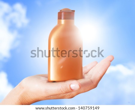 Hand holding plastic bottle of sun lotion against blue sky.