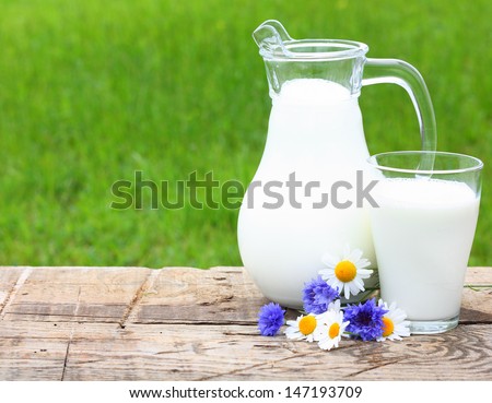 Milk jug and glass on wooden desk with chamomiles.