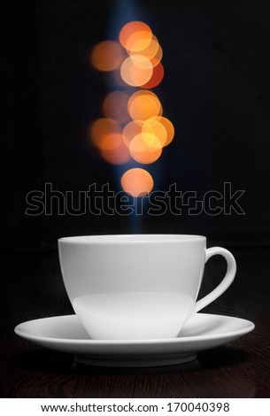 Coffee cup with smoke and abstract bokeh against black wall.