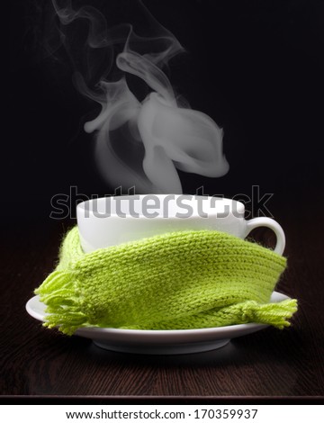Coffee cup or hot tea with smoke in green scarf on wooden table