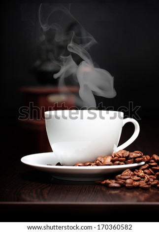 Coffee cup with smoke, grinder and grain against black wall.
