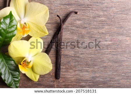 Vanilla pods and orchid flowers on wooden background